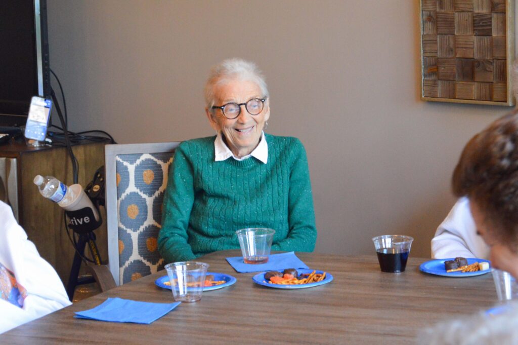 A smiling resident enjoys snacks and drinks at Inspirations of Mount Washington, highlighting the social atmosphere of senior living in Taylorsville.