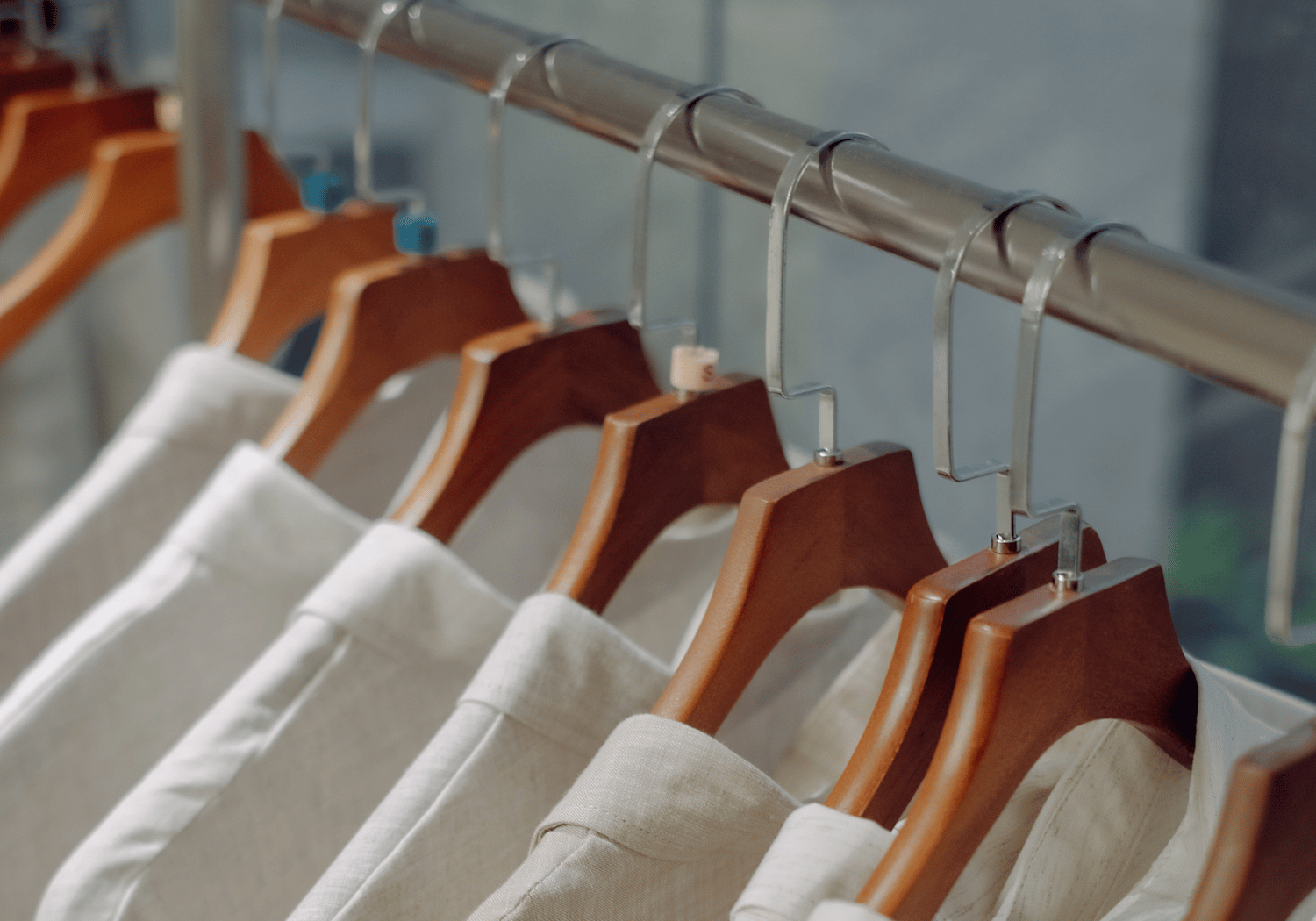 Beige shirts on wooden hangers hanging from a metal rod in a clothing store or closet.