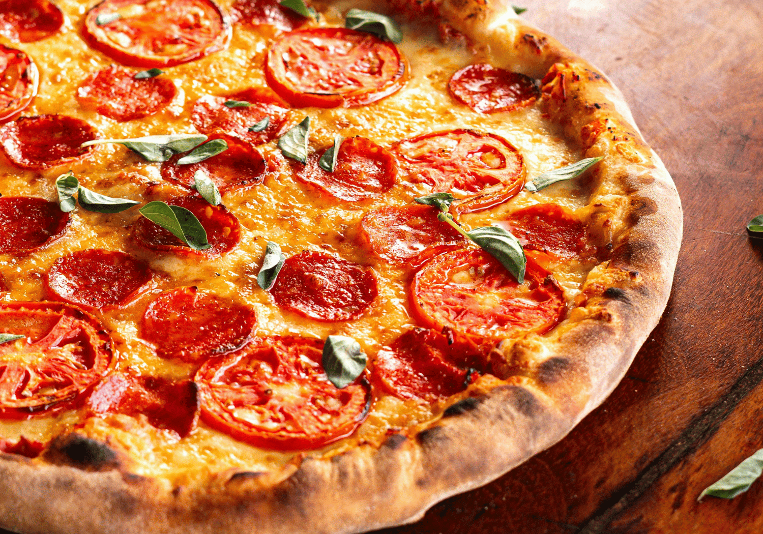 Pepperoni pizza with melted cheese and fresh basil on a wooden board surface.